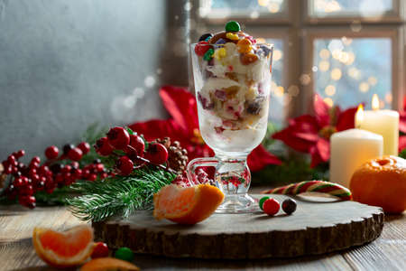 Christmas dessert. Ice cream with winter spices, candied fruits, sweets and caramel in a glass on the background of a window with Christmas lights. Concept of Christmas or winter holidays.の写真素材