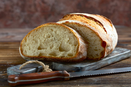 Slice of artisanal sourdough bread cut from a loaf on a wooden cutting board close-up, selective...