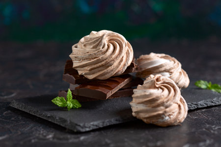 Swiss meringue in the form of spiral with dark chocolate on a slate plate close-up, selective focus....
