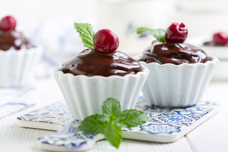 Chocolate cupcakes with ganache in porcelain molds decorated with cherries and fresh mint, selective focus.の写真素材