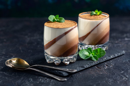 Panna cotta with chocolate and vanilla in glass glasses on a slate stand. Layered dessert.の写真素材