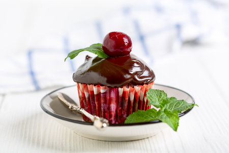 Chocolate cupcake with ganache and cherries in paper mold, served with fresh mint, selective focus.の写真素材