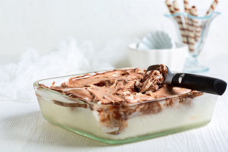 Ice cream spoon and homemade chocolate and vanilla ice cream in a glass container.の写真素材