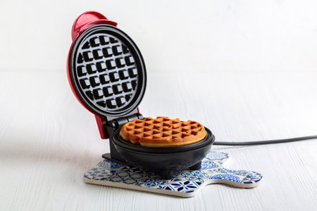 Small waffle maker for making round waffles on a white wooden background. Copy space.の写真素材