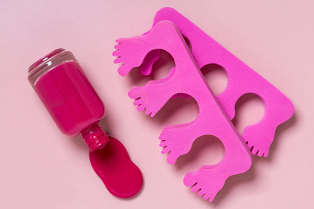 vibrant pink nail polish bottle lies next to pink foam toe separators on a pink background, perfect...