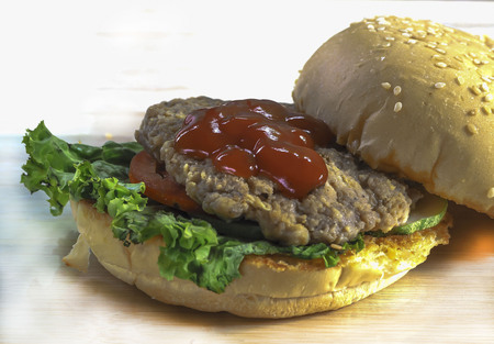 Close up of homemade cheese burger with grilled bacon and fresh vegetable, slice of tomato and lettuce on wooden boardの写真素材