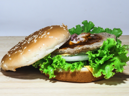 Close up of homemade cheese burger with grilled bacon and fresh vegetable, slice of tomato and lettuce on wooden boardの写真素材