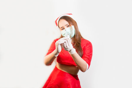 An Asian woman wearing a red Christmas Santa Claus costume wears a medical mask in hand holding vaccine. isolated on a white backgroundの写真素材
