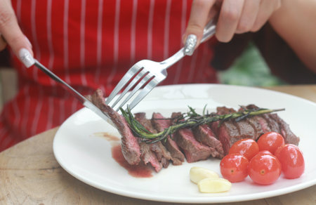 A steak on a white plate ready to eat, garnished with red tomatoes and rosemary for flavor.の写真素材