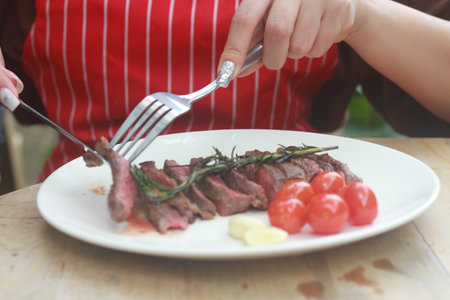 A steak on a white plate ready to eat, garnished with red tomatoes and rosemary for flavor.