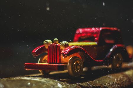 Vintage toy car under the rain on the road. Miniature Car Toy in Rain. Red and yellow vintage car on...