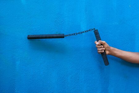 Boy holding Nunchaku on his hand isolated on Blue background. Black nunchaku training for beginner. Hot Tactical Gear Martial Arts Equipments.の写真素材