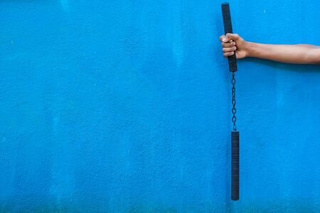 Boy holding Nunchaku on his hand isolated on Blue background. Black nunchaku training for beginner....