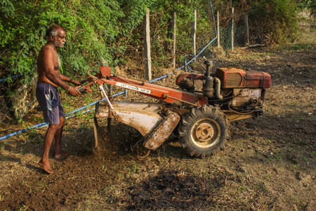 Old Perungalathur, Chennai, India. 25-April-2020: Framer Handing Mini tractor on the field and Planting root crops for agricultural harvest & cultivate in the urban area.Tiller tractor.のeditorial素材