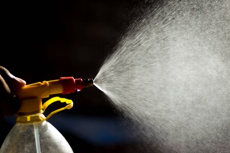 Air pump water spray bottle. close up of a spraying water drops isolated on black background.
