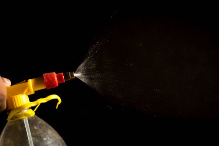 Air pump water spray bottle. close up of a spraying water drops isolated on black background.の写真素材