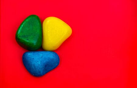 Multi color Natural Pebbles Green, Blue and yellow stone isolated on red background with space for copy text and words. Colorful Natural Pebbles stone isolated. Colorful Sea stones. RGB color stones.の写真素材