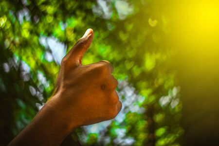 Boy hand with thumb upwards on Heart Bokeh nature background. Showing Positive thumbs up Bokeh background - closeup shot.の写真素材