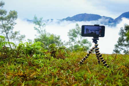 Smart Mobile phone holding on mini Tripod stand at beautiful landscape. Mobile tripod Stock images.の写真素材