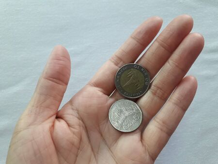 The woman's hand and Thai baht coins are in the hands on a white cloth background.