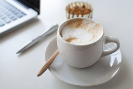 a cup of coffee and laptop on a white deskの写真素材