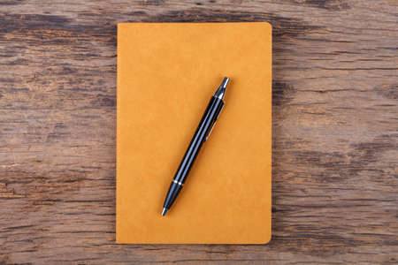 Blank yellow note pad with pen on wood background