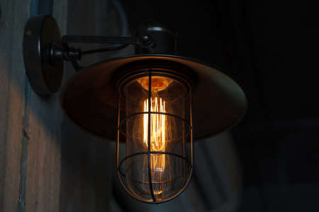 A classic Edison light bulb on old wall background switched on.