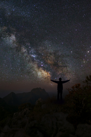 Landscape with milky way, Night sky with stars and silhouette of a standing happy man on the mountain, Long exposure photograph, with grainの写真素材