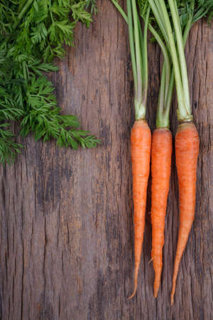 Bunch of fresh carrots with green leaves over wooden backgroundの写真素材