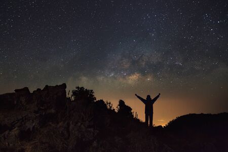 Milky way galaxy and silhouette of a standing happy man at Doi Luang Chiang Dao with Thai Language top point signs. Long exposure photograph.With grainの写真素材