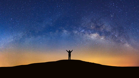 Panorama landscape with milky way, Night sky with stars and silhouette of a standing sporty man with raised up arms on high mountain.の写真素材