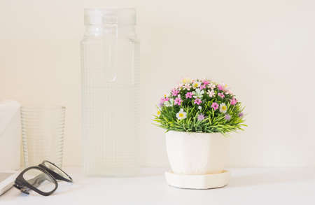 Plastic flower bouquet  in a pot placed on a white wooden in a bed room
