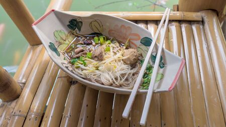 Rice vermicelli in thicken soup with sliced pork and pork ball on bamboo chairの写真素材