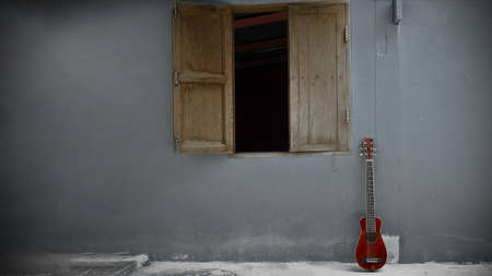 A small red guitar leaning against an old cement wall in vintage toneの写真素材