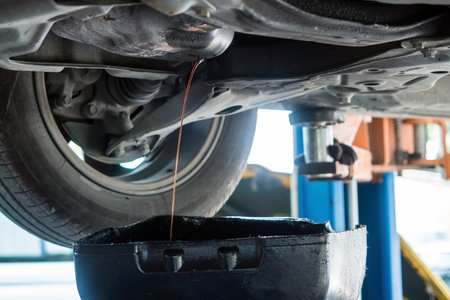 Auto mechanic unscrews engine oil drain plug so that the old used oil flows out of the panの写真素材