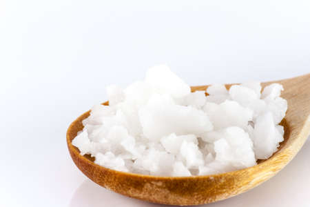 White scrub salt on a wooden spoon against a white backdrop.の写真素材