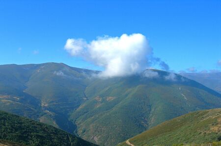 smokey white cloud floats over green mountain peakの写真素材