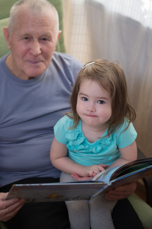 Cute little girl reading a book with her grandfatherの写真素材