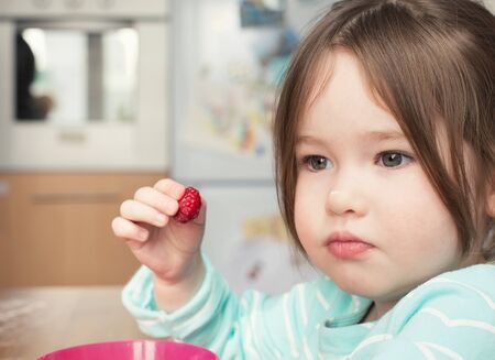A cute little girl holding a raspberryの写真素材