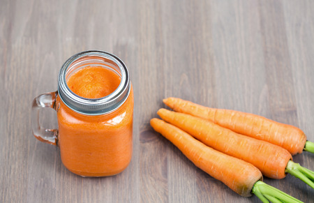 Healthy carrot smoothie in a mason jar with carrots on wooden background. Shallow dofの写真素材