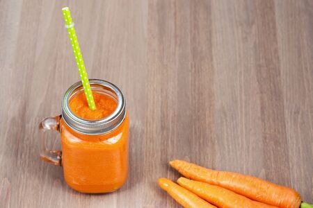 Healthy carrot smoothie in a mason jar with green parsley on wooden background. Shallow dofの写真素材