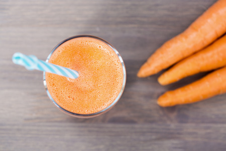A glass of healthy carrot smoothie with carrots on wooden backgroundの写真素材