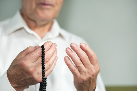 Praying hands of an old man holding rosary beads. Selective focus