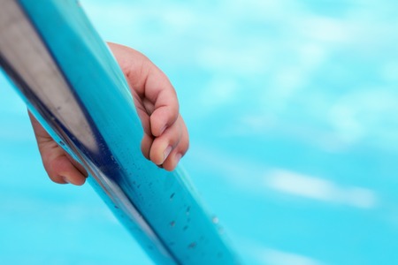 Child's hand holding a handrail in a swimming poolの写真素材