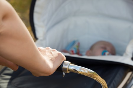A woman hand strolling sleeping boy in a baby carriage in a park