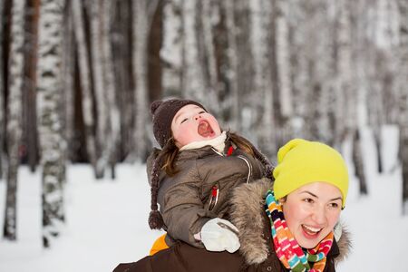 A little girl catching snowflakes sitting on mother's back. Selective focus on a girlの写真素材