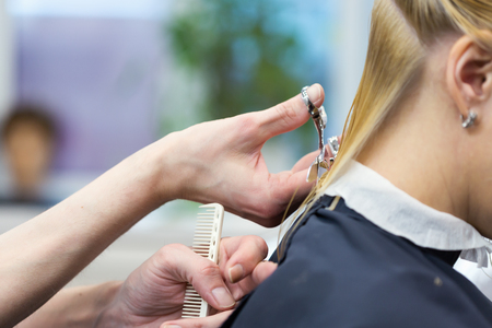 A hairdresser making haircut for a blonde female client in hairdressing salon. Selective focusの写真素材