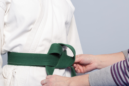 Hands of a parent who helps a child to tietie a green belt for martial arts trainingの写真素材