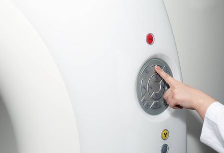 A female doctor's hand pushing control button on CT scanner. Computerised tomographyの写真素材