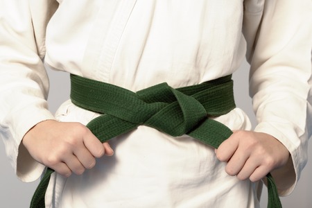 Hands tightening green belt on a teenage dressed in kimono for martial arts. Sepia toningの写真素材